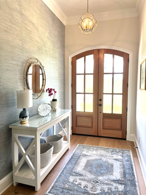 Entryway with blue grass wallpaper, a white console table, mirror and artwork