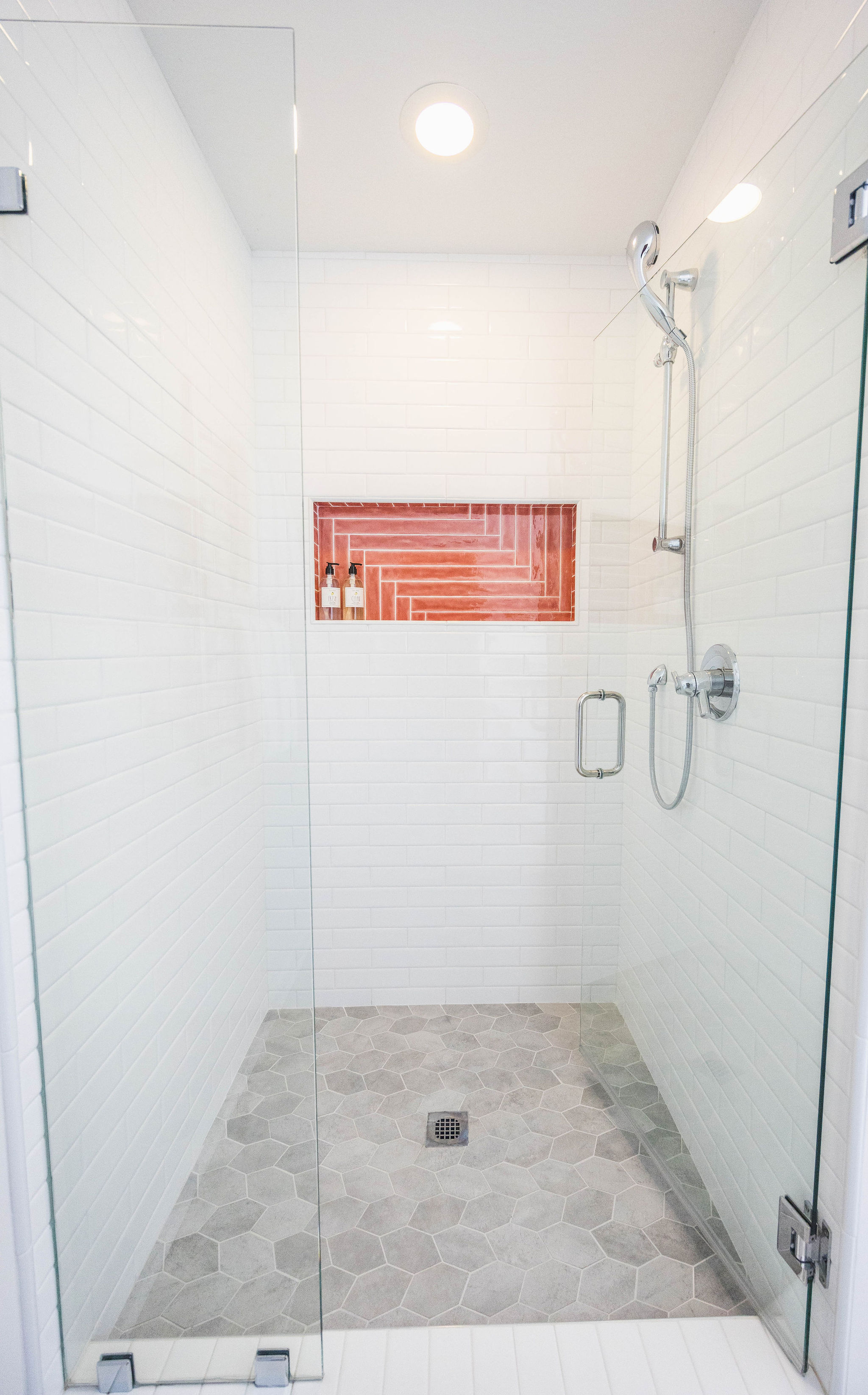 Shower with white subway tile and coral red shower niche and chrome fixtures