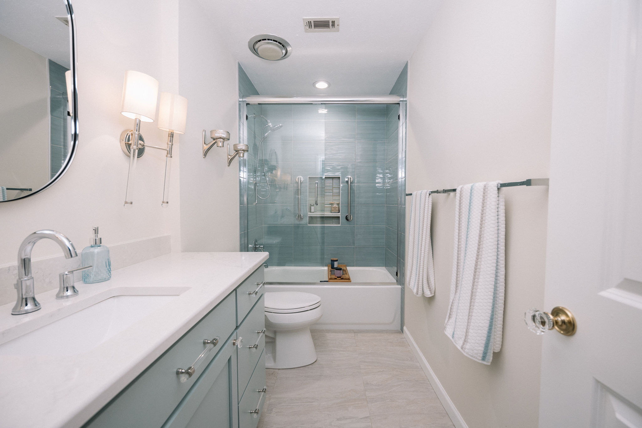 coastal guest bathroom with blue and green tile, blue vanity and chrome fixtures