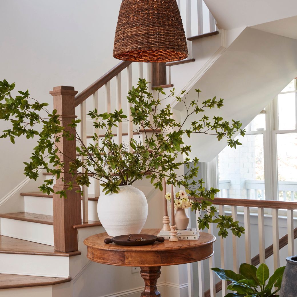 white vase with greenery in it. nude color candles and wicker pendant light
